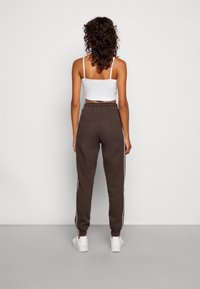 Pantaloni joggers marroni in cotone con strisce bianche laterali, vita elastica e caviglie elasticizzate, abbinati a un crop top bianco aderente.