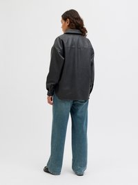 Black faux leather jacket with a relaxed fit, wide sleeves, and a collar. Paired with loose denim jeans in a light blue wash.
