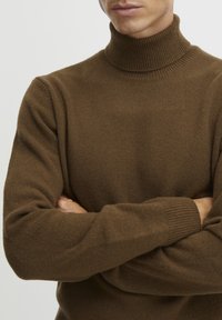 Pull à col roulé marron en tissu texturé. Comprend des poignets et un col côtelés. Coupe ajustée avec manches longues.