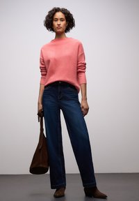 Vaaleanpunainen neulottu paita korkealla kauluksella, yhdistetty korkeavyötäröisiin sinisiin leveälahkeisiin farkkuihin. Ruskea mokkanahkainen käsilaukku ja nilkkurit täydentävät asun.