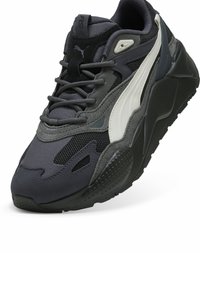 Puma sneakers featuring a mix of dark gray and black materials, mesh accents, a textured sole, and a distinctive white swoosh design.