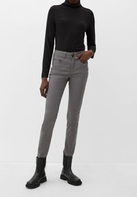 Šedé slim-fit kalhoty s hladkým povrchem, zapínáním na knoflík a zip, a předními kapsami, spárované s upnutým černým rolákem a černými kotníkovými botami.