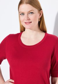 Červený triko s krátkým rukávem z pleteniny, kulatým výstřihem, hladkou texturou a přiléhavým střihem, které zdůrazňuje hladký povrch a rovnoměrnou barvu.