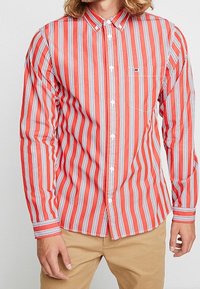 Camicia button-up a righe rosse e bianche con colletto, taschino sul petto, e maniche lunghe con polsini a contrasto. Texture liscia.