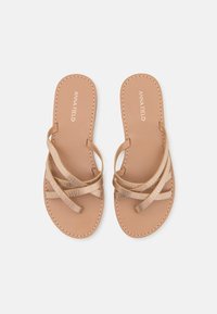 Bruna platta sandaler med korsade remmar som har en texturerad mönster. Slät sula med sydda kanter. Logotyp på innersulan.