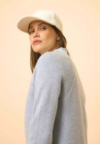 Lichtblauwe trui van zachte stof, met een ontspannen pasvorm en ribbeldetails. Gecombineerd met een crèmekleurige corduroy pet.