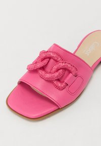 Pink leather slide sandal with a large twisted strap detail, flat sole, and a smooth texture. Features branding on the insole.