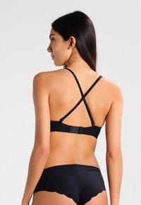 Sort bh med krydsryg, justerbare hægter og en glat tekstur. Har et enkelt design, der egner sig til forskellige outfits.
