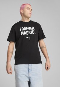 Melna kokvilnas T-krekls ar lieliem baltiem burtiem "FOREVER. MADRID." un mazu baltu Puma logotipu. Īsas piedurknes un brīvs griezums.