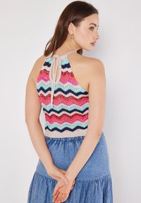 Top sin mangas de punto con un patrón ondulado en rosa, azul y navy. Presenta un lazo en la espalda y una tela texturizada. Combinado con una falda de mezclilla azul.