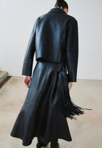 Zwart lederen jack en jurk ensemble met een cropped jack en een uitlopende rok met lange franjes aan de taille. Gladde textuur.