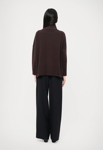 Un pull à col roulé surdimensionné marron en tricot doux, associé à un pantalon noir à taille haute et jambes larges, vu de dos.