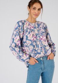 Blusa floral en azul, con mangas abullonadas y cierre de botones en la parte delantera. El estampado incluye flores rosas y moradas, con una tela suave y ligera.