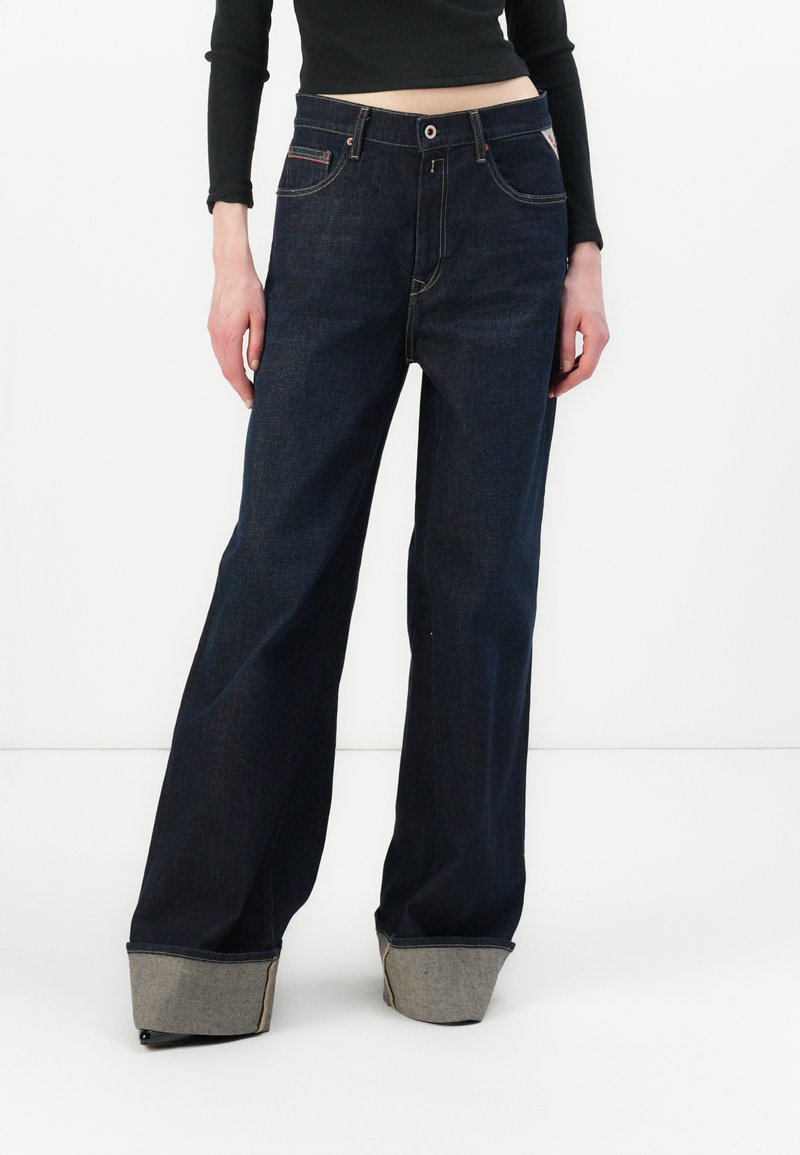 Wijde donkere denim jeans met een hoge taille. Voorzien van een knoopsluiting, zakken aan de voorkant en opgerolde manchetten met contrasterende stof.
