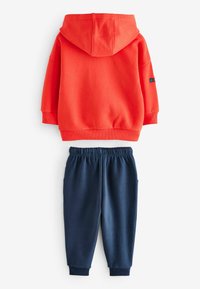 Rød cotton sweatshirt med hætte og ribbede manchetter. Marineblå sweatpants med elastisk talje og tapered ankler.