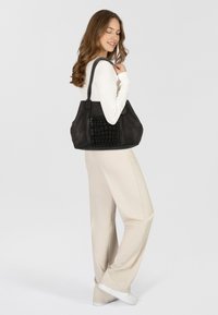Bolso de cuero negro con un frente con relieve de cocodrilo. Tamaño grande, forma versátil, doble asa y un acento de hardware plateado en el frente.