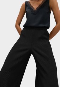 Top de satén negro sin mangas con borde de encaje en el escote, combinado con pantalones anchos texturizados de canalé en negro.