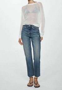 Top a maniche lunghe bianco in rete sopra un paio di jeans blu a gamba dritta leggermente accorciati, con sandali neri con cinturini. Abbigliamento casual.