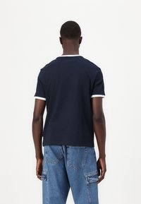 Camiseta de manga corta azul marino con cuello y puños de canalé blancos, hecha de algodón. La parte posterior presenta un diseño limpio y un dobladillo recto.