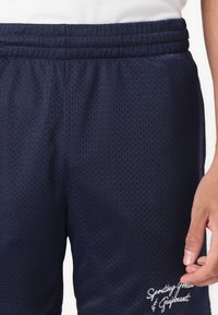 Dunkelblaue Netz-Athletik-Shorts mit einem gewebten elastischen Bund. Verziert mit dekorativem, weißem, gesticktem Text am Saum.