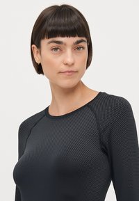 Svart långärmad topp med en strukturerad mönster, med rund halsringning och raglanärmar, tillverkad av ett stretchigt, andningsbart material.