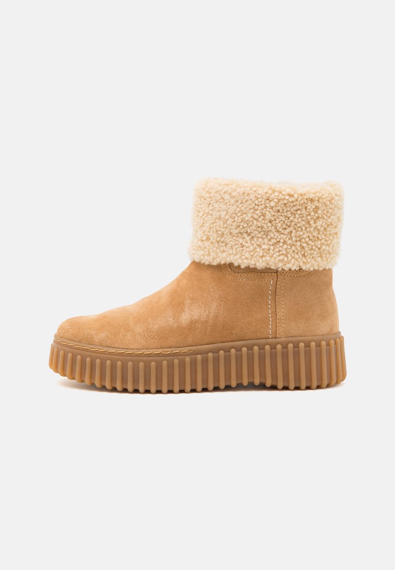Botines de ante en tono arena con un suave puño de crema, suela de goma texturizada y detalles acanalados. Punta redondeada y costuras laterales.