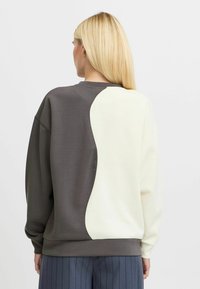 Two-tone sweatshirt with grey and cream panels. Soft fabric, oversized fit, ribbed cuffs and hem. Smooth texture with a contrasting design.