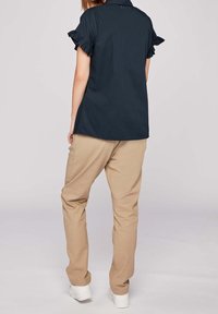 Mörkblå kortärmad topp med volangärmar, i kombination med beige byxor. Modellen bär vita sneakers. Enkel, avslappnad design.