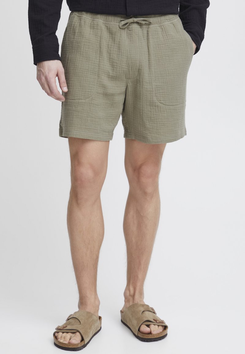 Olivengrønne shorts af tekstureret stof med elastisk talje og snøre samt to forlommer. Bæres med brune sandaler.