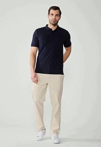 Polo de manga curta azul-marinho com textura ribete horizontal, combinado com calças beje claras e ténis brancos.
