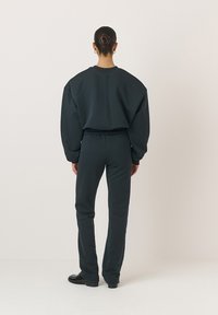 Ciemnozielony sweatshirt i pasujące spodnie wykonane z miękkiego materiału; luźny krój z obniżonymi ramionami i zwężającymi się nogawkami; gładka tekstura, minimalne detale.