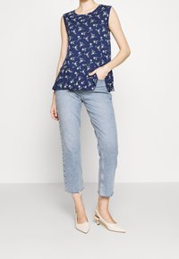 Navy floral peplum top with short sleeves, paired with light blue high-waisted jeans and nude slingback heels. Textured floral pattern evident.