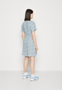 Robe florale bleue à manches courtes, taille cintrée, jupe évasée. Associée à des baskets bleu clair et des chaussettes blanches. Design simple et décontracté.