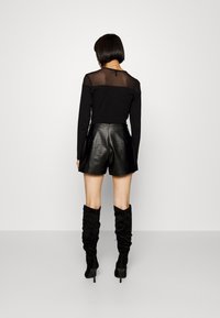 Černé dlouhé rukávy top s průhledným síťovaným výstřihem, spárovaný s vysokými černými koženými kraťasy a černými semišovými botami po kolena.