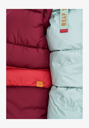 Nahaufnahme von dunkelroten und hellblauen gesteppte Jacken mit orangefarbenen und roten Etiketten, die die Stoffstruktur und Nähte zeigen.