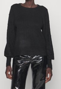 Maglione nero a maglia con scollatura arrotondata e maniche a sbuffo, con perline nere lungo le maniche. Abbinato a pantaloni in ecopelle nera lucida.