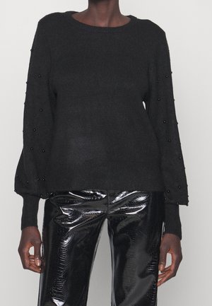 Maglione nero a maglia con scollatura arrotondata e maniche a sbuffo, con perline nere lungo le maniche. Abbinato a pantaloni in ecopelle nera lucida.