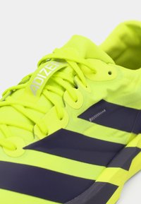 Jasnozielony but do biegania z ciemnoniebieskimi akcentami, wyposażony w fakturowaną cholewkę, wyraźny system sznurowania oraz logo "ADIZERO" na języku.