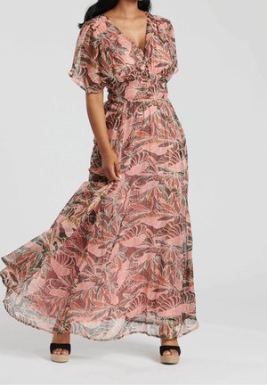 Frau trägt ein pink-braunes Maxikleid mit Blumenmuster, Puffärmeln und schwarzen Plateau-Sandalen, hält den Saum des Kleides fest.