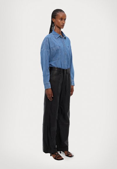 Cămașă din denim cu două buzunare pe piept, de culoare albastru deschis. Pantaloni largi din piele neagră, cu coase vizibile. Sandale plate negre.