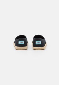 Scarpe slip-on nere in tela con suola in juta, dotate di patch con il logo blu TOMS sui talloni e una finitura testurizzata.