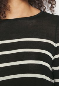 Pull en tricot à rayures noires et blanches avec un col rond, présentant des rayures horizontales et une texture douce. Gros plan sur le tissu.