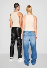 Dva posameznika sta oblečena v bež top tank, črne usnjene hlače in svetlo modre denim hlače, vidna od zadaj. Opazna blagovna znamka je na pasu.