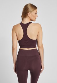 Maroon sportief crop top met racerback ontwerp, voorzien van een gestructureerde stof en een chevronpatroon op de rug. Gecombineerd met bijpassende, hoog geplaatste leggings.