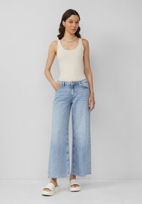 Lichtbeige tanktop, wijdvallende lichtblauwe denim jeans en witte platform sandalen. Glad materiaal, relaxte pasvorm en subtiele wassing.