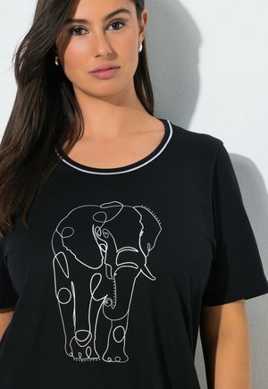 Donna con capelli lunghi e scuri indossa una maglietta nera con un disegno a linea continua bianca di un elefante visto frontalmente.