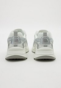 Par de zapatillas deportivas blancas y grises mostradas desde la parte trasera sobre un fondo blanco liso.