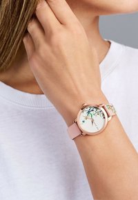 Reloj de pulsera de oro rosa con un dial blanco con patrón floral y una suave correa de cuero rosa, que presenta una caja redonda y marcadores de horas simples.