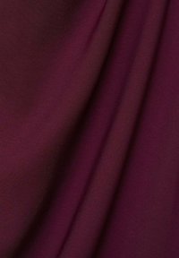 Tissu bordeaux avec une texture lisse et mate, présenté en doux plis qui mettent en valeur son mouvement et son poids.