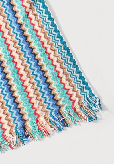 Tissu tissé avec des rayures en zigzag colorées en bleu, rouge, beige et blanc, se terminant par des franges multicolores sur un fond blanc.
